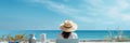 Rear view of young woman, female freelancer in straw hat working on laptop, while sitting on the tropical sandy beach Royalty Free Stock Photo