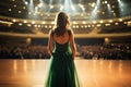 Rear view of a young woman in a green dress standing in front of a stage in a theater, Back view of a girl in a green evening