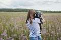 Rear view of young woman holding gray fluffy senior dog in hands on meadow with flowers of fireweed or great willowherb, pet love Royalty Free Stock Photo