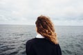 Rear view of young woman looking at overcast sky and gray sea Royalty Free Stock Photo