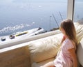 A little girl sits by the window and looks at the ocean. The view from the window to the sea.Rear view of young woman looking at Royalty Free Stock Photo