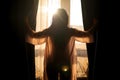 Rear view young woman opens curtains of bedroom window. Young girl is ready for new plans and new challenges. Royalty Free Stock Photo