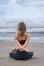 rear view of young woman practicing yoga in lotus pose with arms crossed behind back on seashore Royalty Free Stock Photo