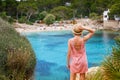 Rear view of a young woman standing on a cliff and looking at Cala Gat beach in Mallorca