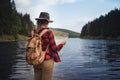 Rear view of young woman standing by lake outdoors in summer nature, using map. Royalty Free Stock Photo