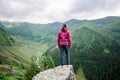 Young female tourist standing on rock edge among magnificent green mountains with grassy slopes Royalty Free Stock Photo