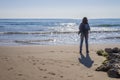 Rear view of young woman wearing casual clothes standing on the beach while looking away in a bright day Royalty Free Stock Photo