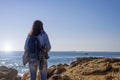Rear view of a young woman wearing casual clothes standing on the beach while looking away in a bright day Royalty Free Stock Photo