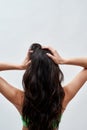 Rear view of young woman wearing green underwear posing against light background, showing off her healthy long dark Royalty Free Stock Photo