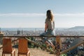Rear view of young woman wearing in stripped t-shirt sitting on high point and looking at cityscape.