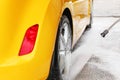 Rear wheel of yellow car being washed with jet water stream in c Royalty Free Stock Photo