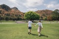 Rear of young asian couple walking holding hands on grass and big tree in park Royalty Free Stock Photo