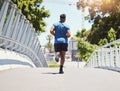 Rearview fit athletic mixed race man running across a bridge in the city for fitness. Young hispanic male outdoors for a Royalty Free Stock Photo