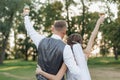 Rearview just married couple of bride in wedding dress with groom in suit toasting drinking champagne wine in park Royalty Free Stock Photo