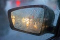 Rearview mirror with drops of water from the rain and a car with headlights. Selective focus, shallow DOF Royalty Free Stock Photo