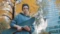 Rebellious young caucasian woman with skateboard standing under the tree with yellow leaves in city park in autumn