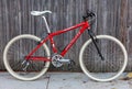 Rebuilt red Specialized Stumpjumper vintage mountain bike with rigid fork and white tires stands against a fence.