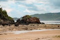 Receding beach with big rocks and hills overgrown with greenery