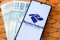 Receita Federal logo on mobile screen and Brazilian money bills