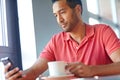 Receiving a text on his coffee break. A young man reading a text message while enjoying a cup of coffee. Royalty Free Stock Photo