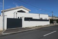 Recent white and gray house with a large protective wall and a dark gray automatic gate