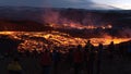 Recently started volcanic eruption at Fagradalsfjall with glowing streams of lava and the silhouettes of people.