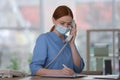 Receptionist with mask talking on phone at countertop in hospital Royalty Free Stock Photo
