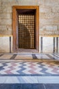 Recessed wooden window with decorated iron grid over stone bricks wall and decorative colorful floor