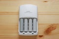 Rechargeable AA battery in a white charger on wooden background.Top view