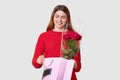 Recieving present is my favourite thing. Smiling pleased young lady opens package, sees something appealing, holds red roses,