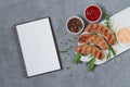 Recipe for grilled BBQ sausages concept. Barbeque sausage with herbs, sauce and spices next to open blank notepad top view on