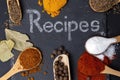 recipes written with white chalk on a black stone tile, surrounded by different spices on wooden spoons. Royalty Free Stock Photo