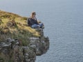 Reckless woman sitting on the edge of a cliff at the Irish west coast