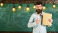 Recommendation concept. Bearded hipster holds book, chalkboard on background. Teacher in eyeglasses recommends book. Man Royalty Free Stock Photo