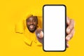 Recommendation. Excited black man holding big smartphone with blank screen through torn yellow paper hole Royalty Free Stock Photo