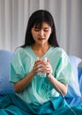 Portrait of recovered young asian woman patient sitting on bed in the hospital holding, looking to a glass of water wanting to Royalty Free Stock Photo