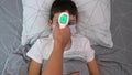 A recovering boy medical protective mask lying in bed and does not want his mother measuring temperature with infrared