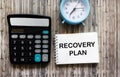 RECOVERY PLAN text in notepad on wooden table near calculator and clock, business concept Royalty Free Stock Photo