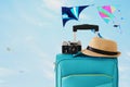 Recreation image of traveler luggage, camera and fedora hat infront of blue sty with flying colorful kites background. holiday and