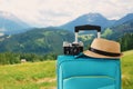 Recreation image of traveler luggage, camera and fedora hat infront of a rural lanscape. holiday and vacation concept