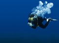 Recreational scuba diver with yellow mask, cloud of bubbles in black neoprene suit taking underwater photo in deep blue water of R