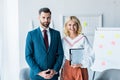 Recruiter with clenched hands and blonde woman with clipboard standing in office