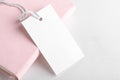 Rectangle white gift tag mockup with white cord, close up on pink book and white background