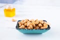 A rectangular blue bowl of whole roasted cashews stands on a white table. A glass jar with honey stands in the background.