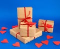 Rectangular box is wrapped in brown paper and tied with a red thin silk ribbon on a blue background, red cut out paper hearts Royalty Free Stock Photo