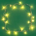 Frame made with Christmas lights on green background, top view. Royalty Free Stock Photo
