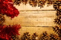 Rectangular frame of pine cones and red tinsel on an old table with a great wooden texture. Ideal for Christmas or autumn Royalty Free Stock Photo