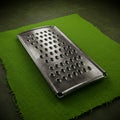 A rectangular metal grater with multiple circular holes lies on a textured green fabric. Royalty Free Stock Photo