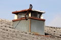 Rectangular rusted chimney with metal mesh protection on all sides covered with partially rusted cover on top