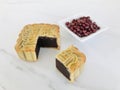 Moon cake with Pure Red Bean Paste cut out a quarter in a with red beans in a sauce dish on white marble background.